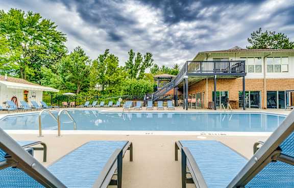 A large outdoor swimming pool with a blue tiled edge and a metal ladder on the left side.