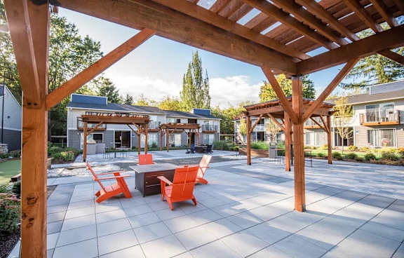 A wooden pergola over a patio with orange chairs and a table.
