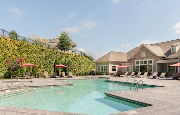A large swimming pool with lounge chairs and umbrellas in front of a house.