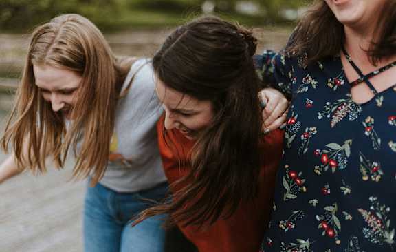 Three women are standing close together, with one woman's arm around the other two.