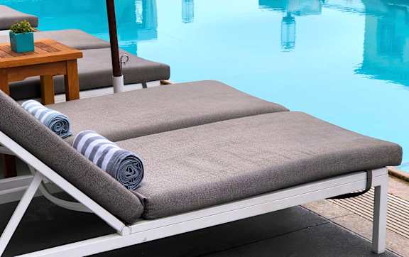 A poolside lounge chair with a rolled-up towel on it.