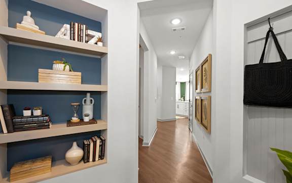 A hallway with a blue wall and a shelf with books and decorations.