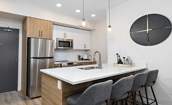 A modern kitchen with a large island and grey chairs.at The Fifth at Palisades, Edmonton, AB, T6V 0N5