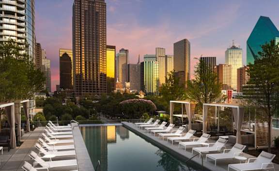A pool with lounge chairs and a city skyline in the background.