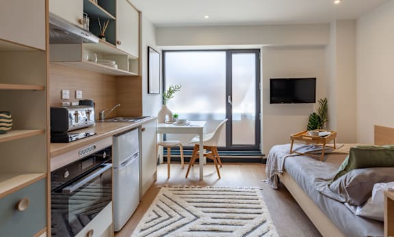 a studio apartment with a bed and a kitchen and a sliding glass door