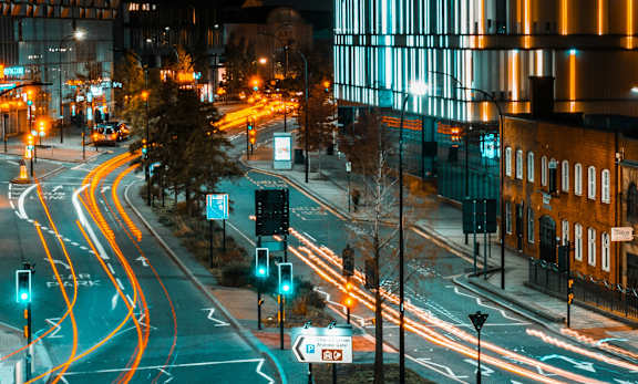 A city street at night with cars driving on the road.