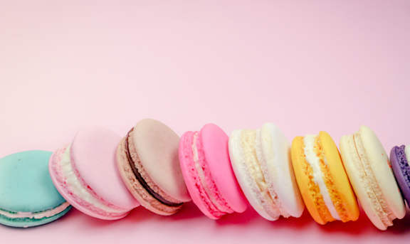 A row of colorful macarons are lined up on a pink background.