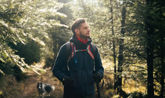 a man with a backpack walking in the woods with a dog