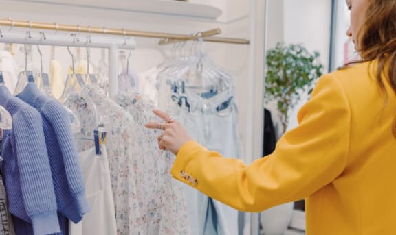 a woman in a yellow suit looking at clothes on a rack