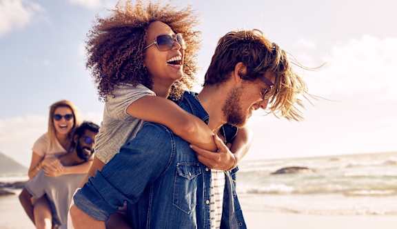 A man is giving a piggyback ride to a woman on a beach.