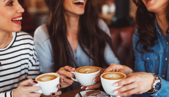 three women holding cups of coffee in a coffee shop