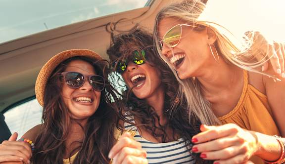 Three women wearing sunglasses and hats are laughing and enjoying themselves in a car