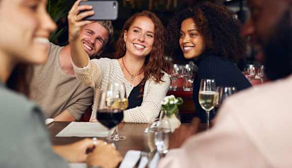 A group of people are sitting around a table taking a selfie.