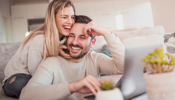 a man and a woman sitting on a couch looking at a laptop