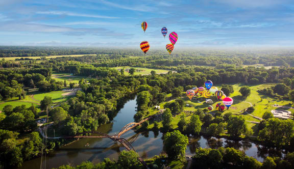 a hot air balloon ride over a park with trees and a river