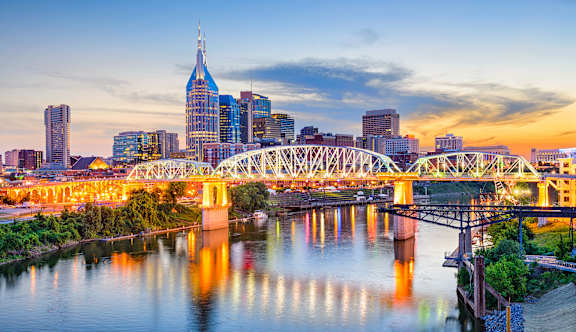 A city skyline at dusk with a bridge crossing a river.