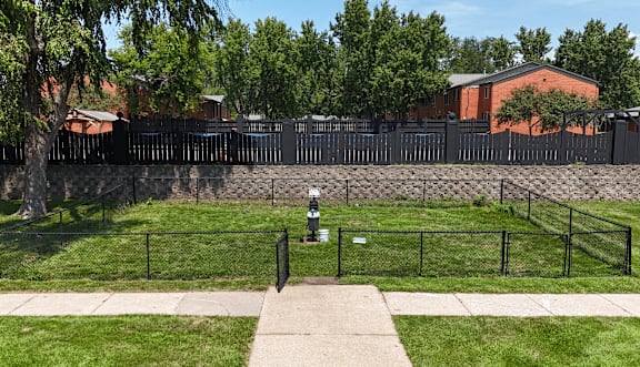 A black fence surrounds a grassy area with a sidewalk and a tree.