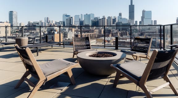 a roof deck with chairs and a fire pit and a city skyline