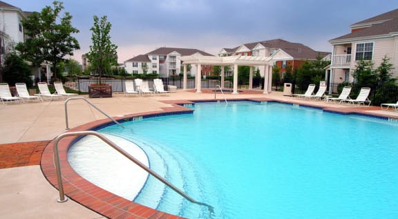 a large swimming pool with chairs and a building in the background