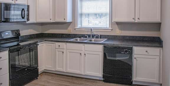A room with a black fridge and wooden flooring.