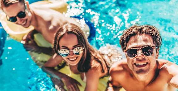 Three people are enjoying a sunny day in a pool.