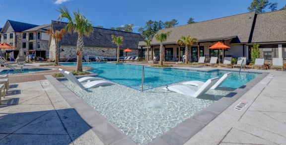 our resort style swimming pool is surrounded by lounge chairs and umbrellas