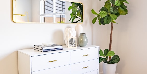 a white dresser with a plant and a mirror in a room