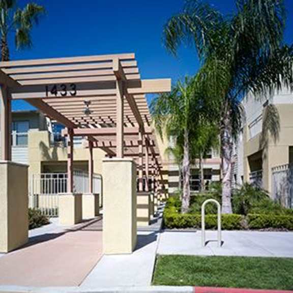 a wooden pergola with the number 1233 is situated in front of a building with a palm tree.