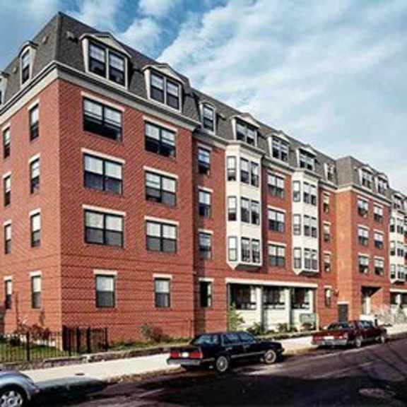 a row of red brick apartment buildings with cars parked in front.