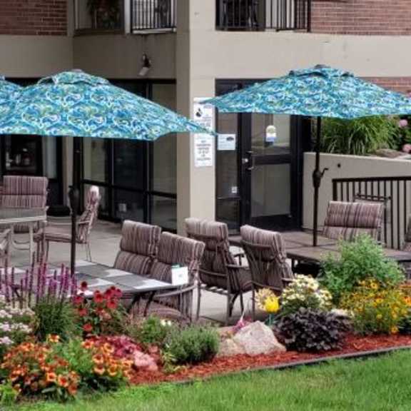 a patio with chairs and umbrellas is surrounded by a flower garden.