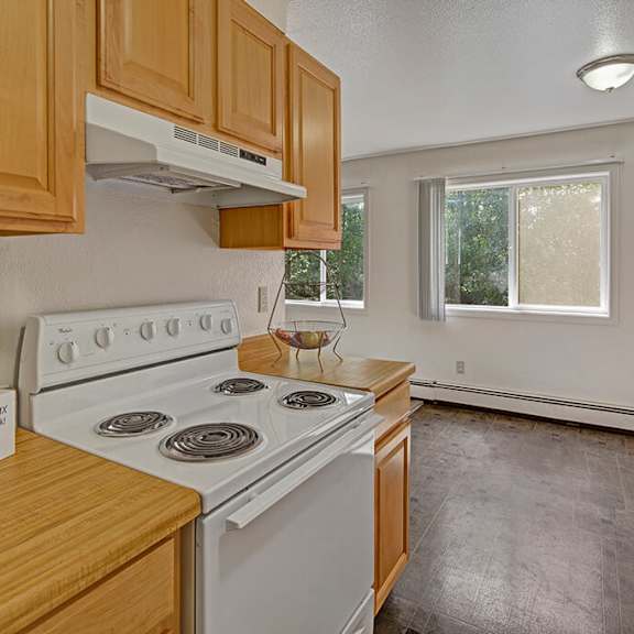 simple kitchen here at the glen apartments with light wood cabinetry, white stove, and box labeled “snack & relax.” bright window, empty fruit bowl, and clean, minimalist decor.