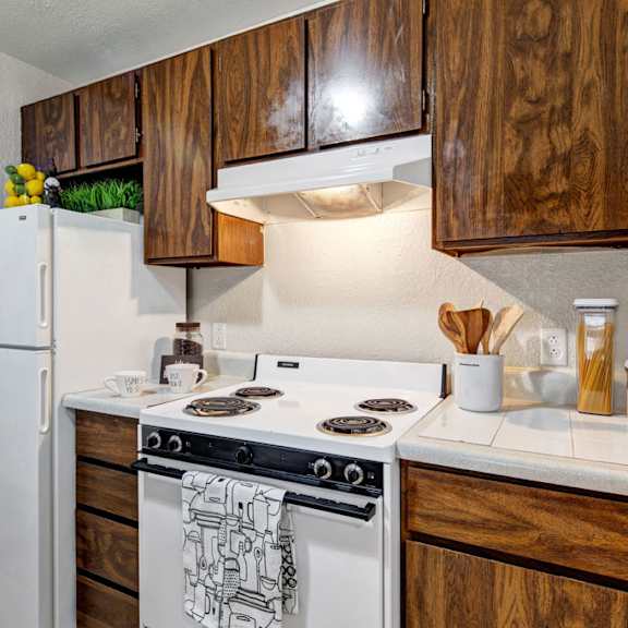 a compact kitchen here at greenbriar apartments with wooden cabinets, white appliances, and decor such as lemons, plants, and utensils. it's cozy and organized.