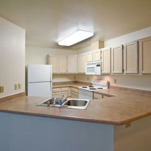 kitchen here at brighton park with wooden cabinets, a white fridge, a stove, and a microwave. a large countertop with a sink extends into the room.