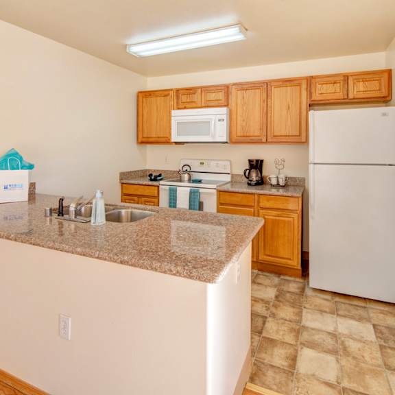 modern kitchen here at timber ridge apartments with wooden cabinets, granite countertops, and white appliances including a fridge and microwave. bright, clean, and organized.