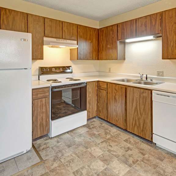simple kitchen here at brighton woods apartments with wooden cabinets, white appliances including a fridge, stove, and dishwasher. neutral tones create a clean, functional space.