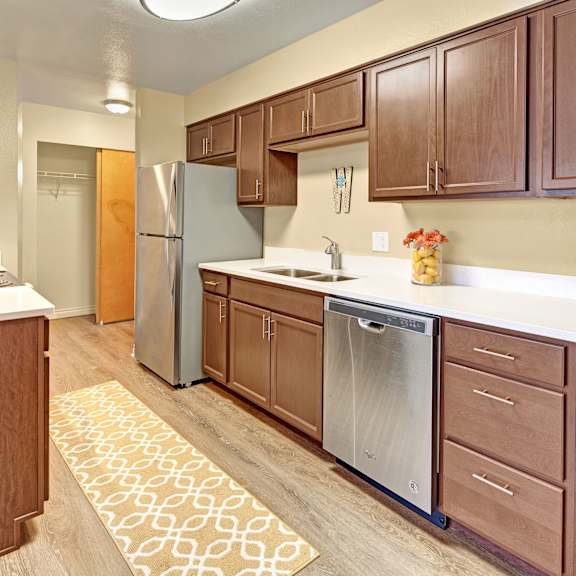 a modern kitchen here at century plaza with wooden cabinets, stainless steel appliances, and a light countertop. a patterned rug adds warmth, while decorative items create a cozy feel.