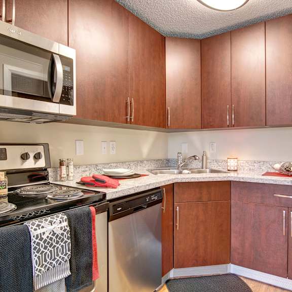 modern kitchen here at 3600 brentwood apartment homes with wooden cabinets, stainless steel appliances, and granite countertops. includes a stove, microwave, sink, and decorative items. cozy ambiance.