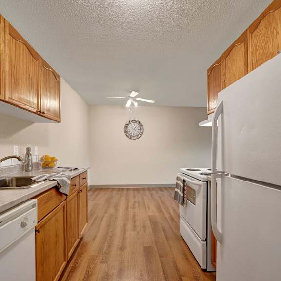 kitchen here at cambridge west apartment homes with wooden cabinets, white appliances, and marble countertop. a clock and ceiling fan are on the back wall, creating a clean, inviting atmosphere.