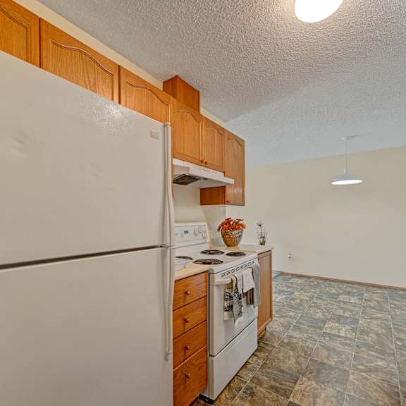 simple kitchen here at sol terrace apartment homes with wooden cabinets and gray-tiled floor. features a white fridge, stove, and a countertop with a basket of flowers, under warm lighting.