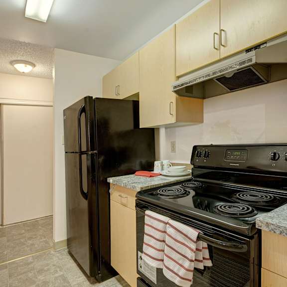 compact kitchen here at sterling place apartment homes with a black stove and refrigerator, wooden cabinets, and a gray countertop. striped towels hang on the oven, creating a cozy feel.