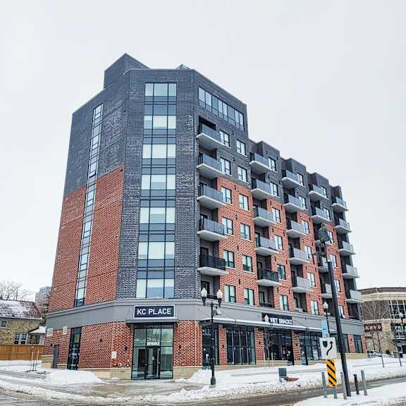 a tall building with a red brick base and a black top with the words kc place on it.
