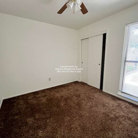 a room with a brown carpet and a ceiling fan.