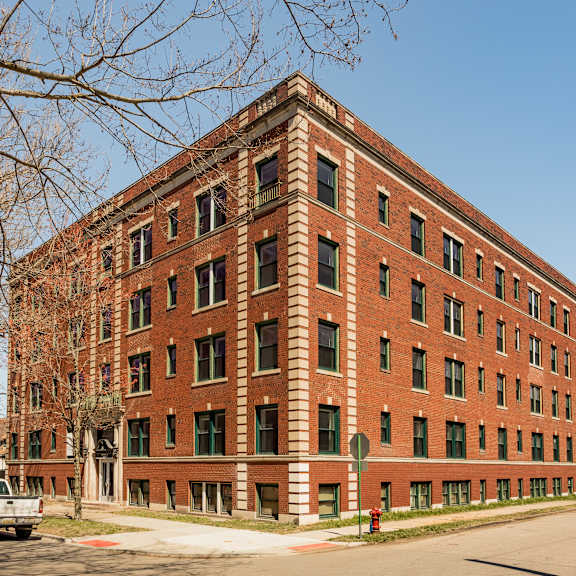 a red brick building with green trim and a parking lot in front.
