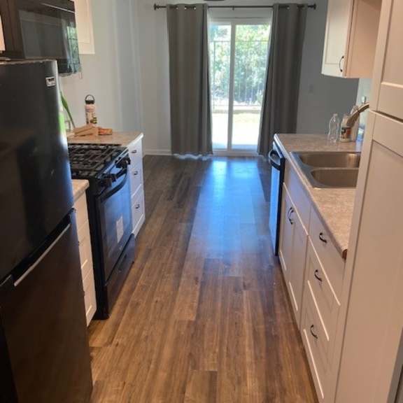 a kitchen with a black fridge and wooden floors.