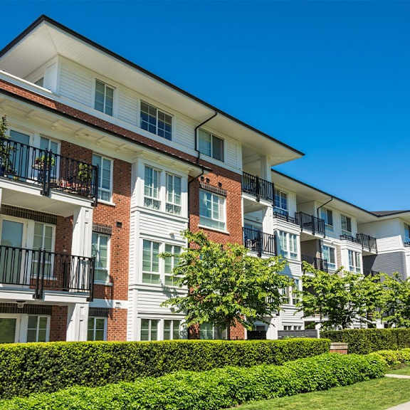 a row of apartment buildings with balconies and green hedges in front.