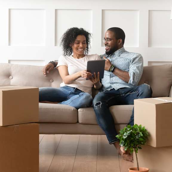 A couple sitting on a couch surrounded by cardboard boxes, possibly moving into a new home. at Park Lamont Apartments & Townhomes, Ohio