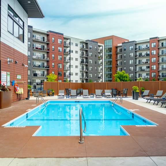 a large swimming pool surrounded by lounge chairs in front of apartment buildings.