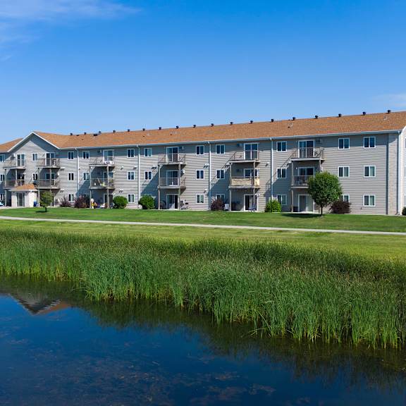 a large building with a grey facade is situated next to a body of water with green vegetation.