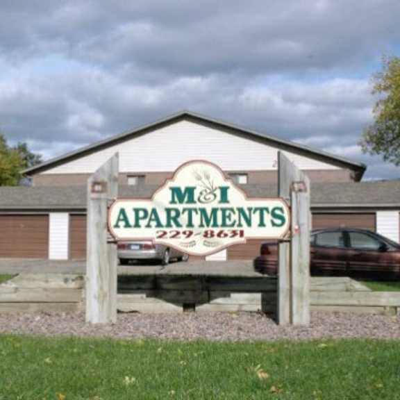 a sign for m&i apartments stands in front of a building.