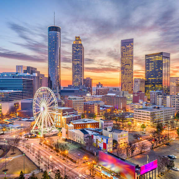 A cityscape at dusk with a Ferris wheel in the foreground.